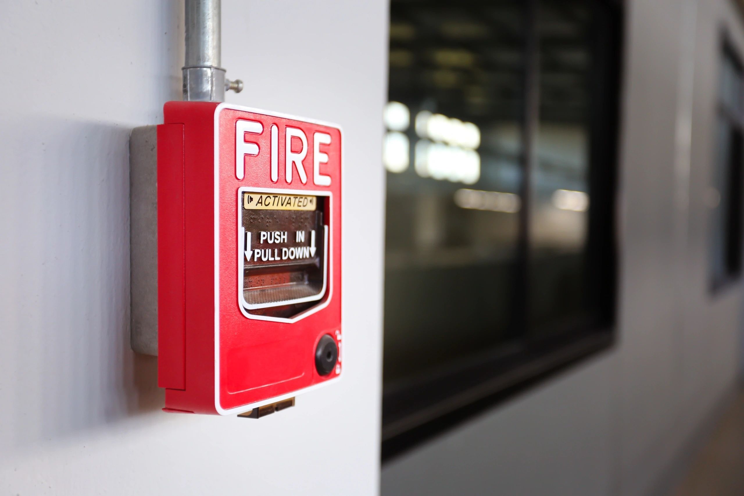 Red fire alarm pull station on white wall