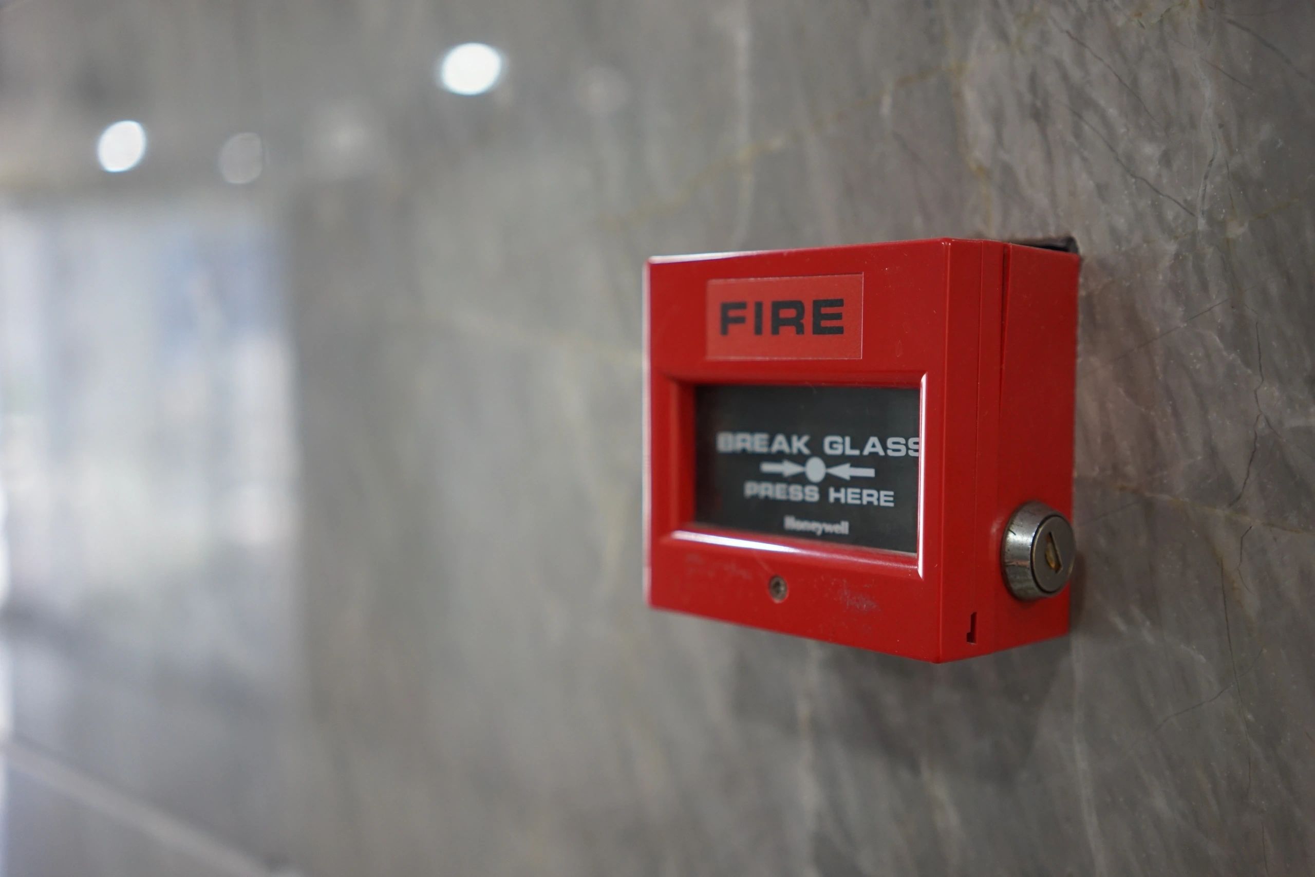 Red fire alarm break glass call point on concrete wall